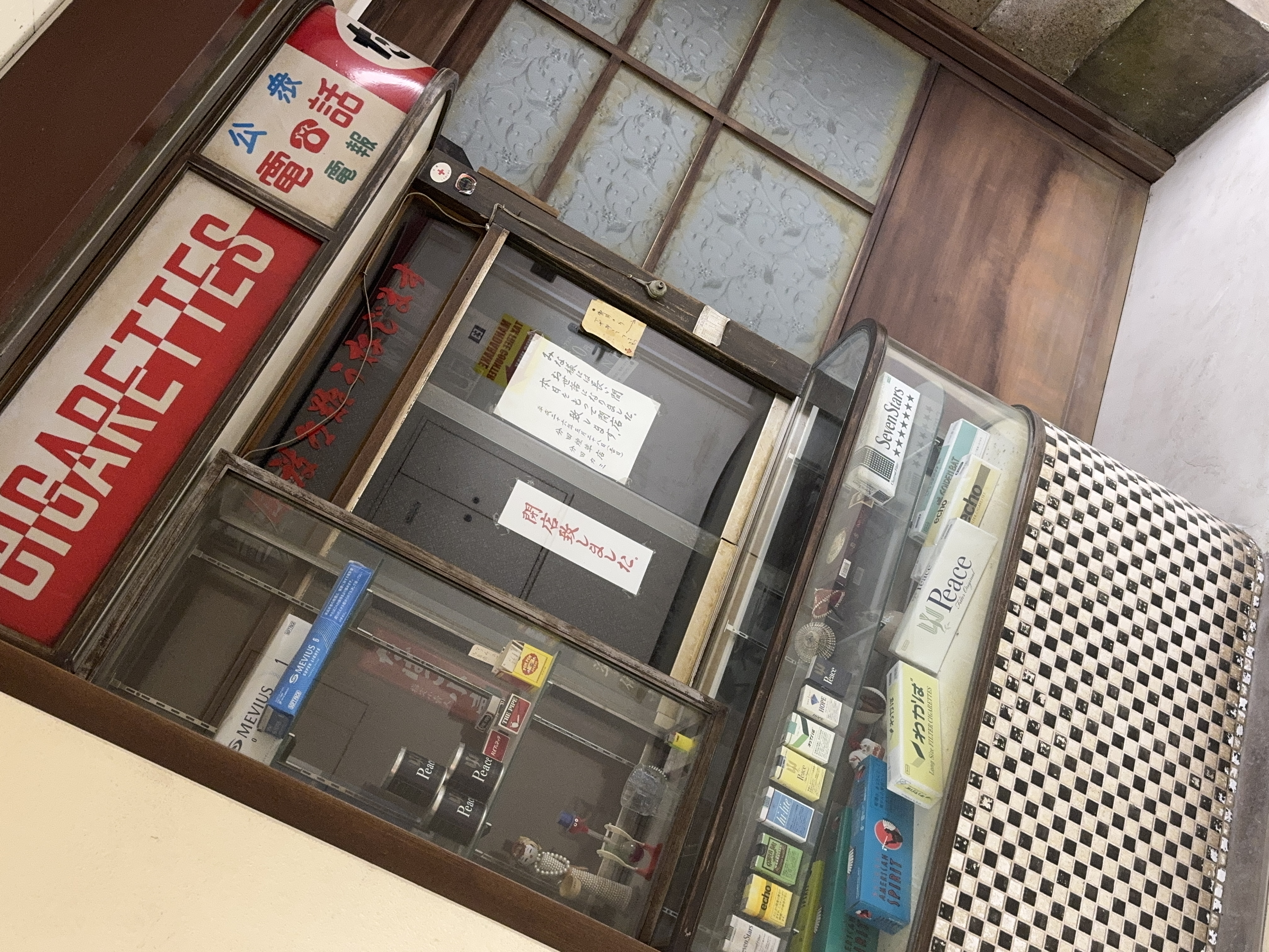 タバコの陳列と公衆電話の看板が残り、閉店致しましたと張り紙があるタバコ屋