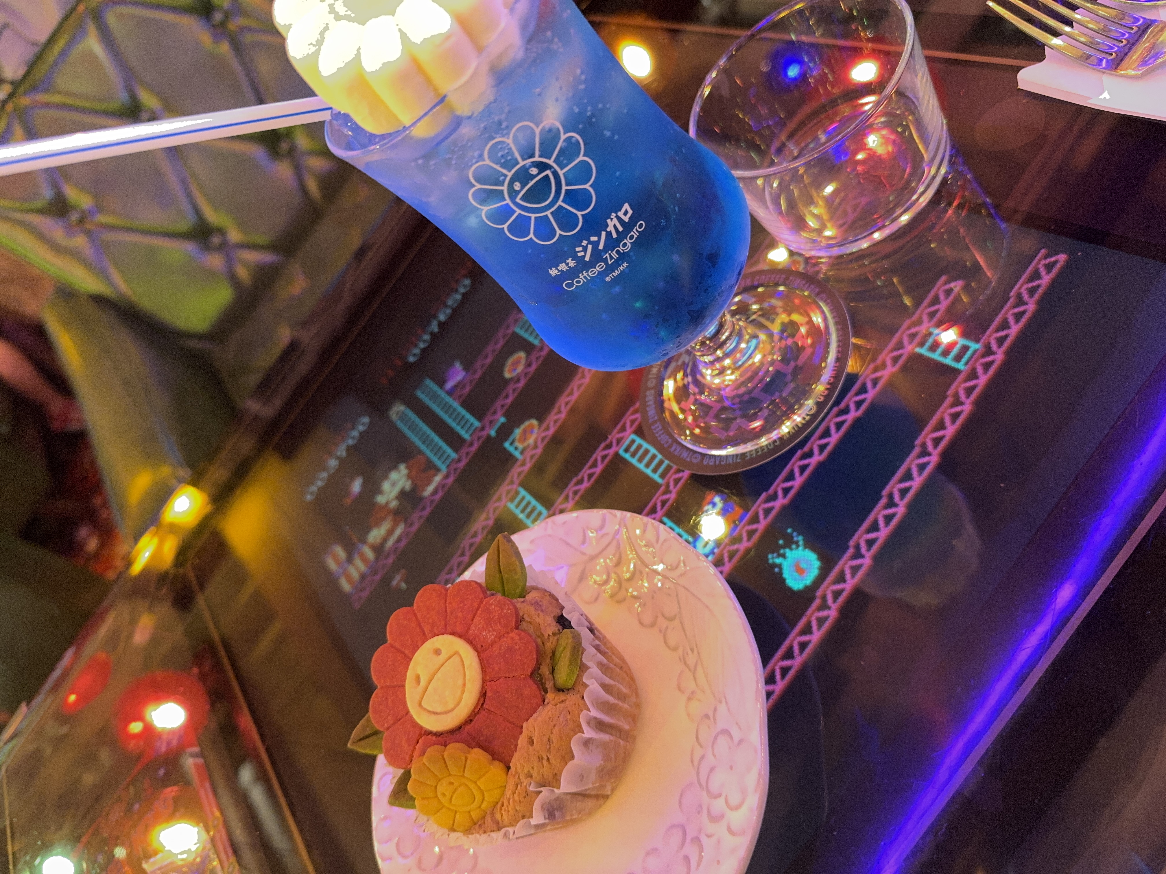 レトロゲームが映るテーブルに置かれた青いクリームソーダと花の形のお菓子